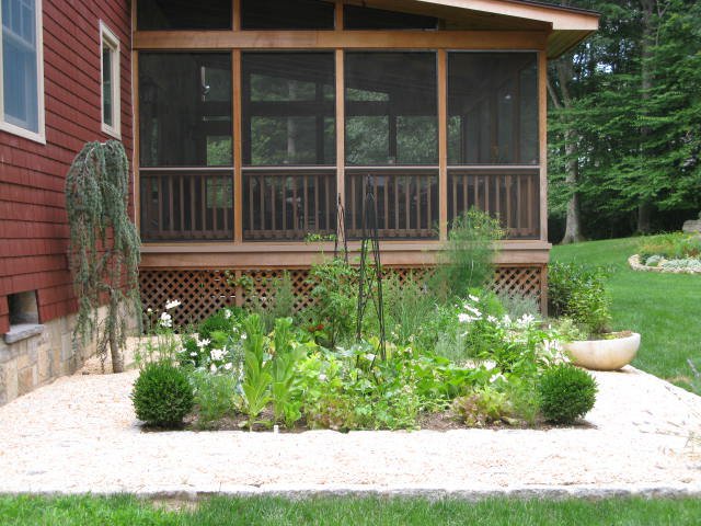 Herb and vegetable garden bed with a gravel path by a screened porch