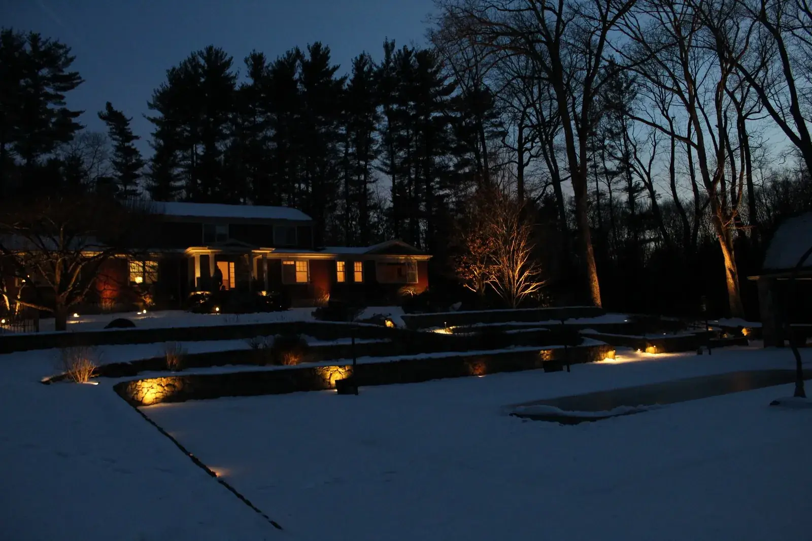 Uplighting on a fieldstone wall and steps at night, with snow in the garden