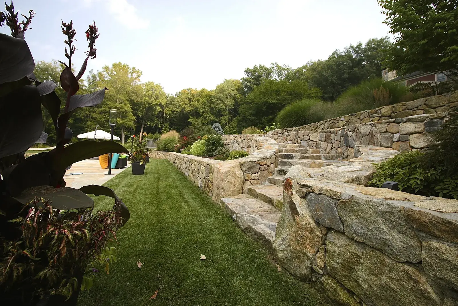 Fieldstone retaining walls and stone steps beside a lawn, built by BREN Landscaping